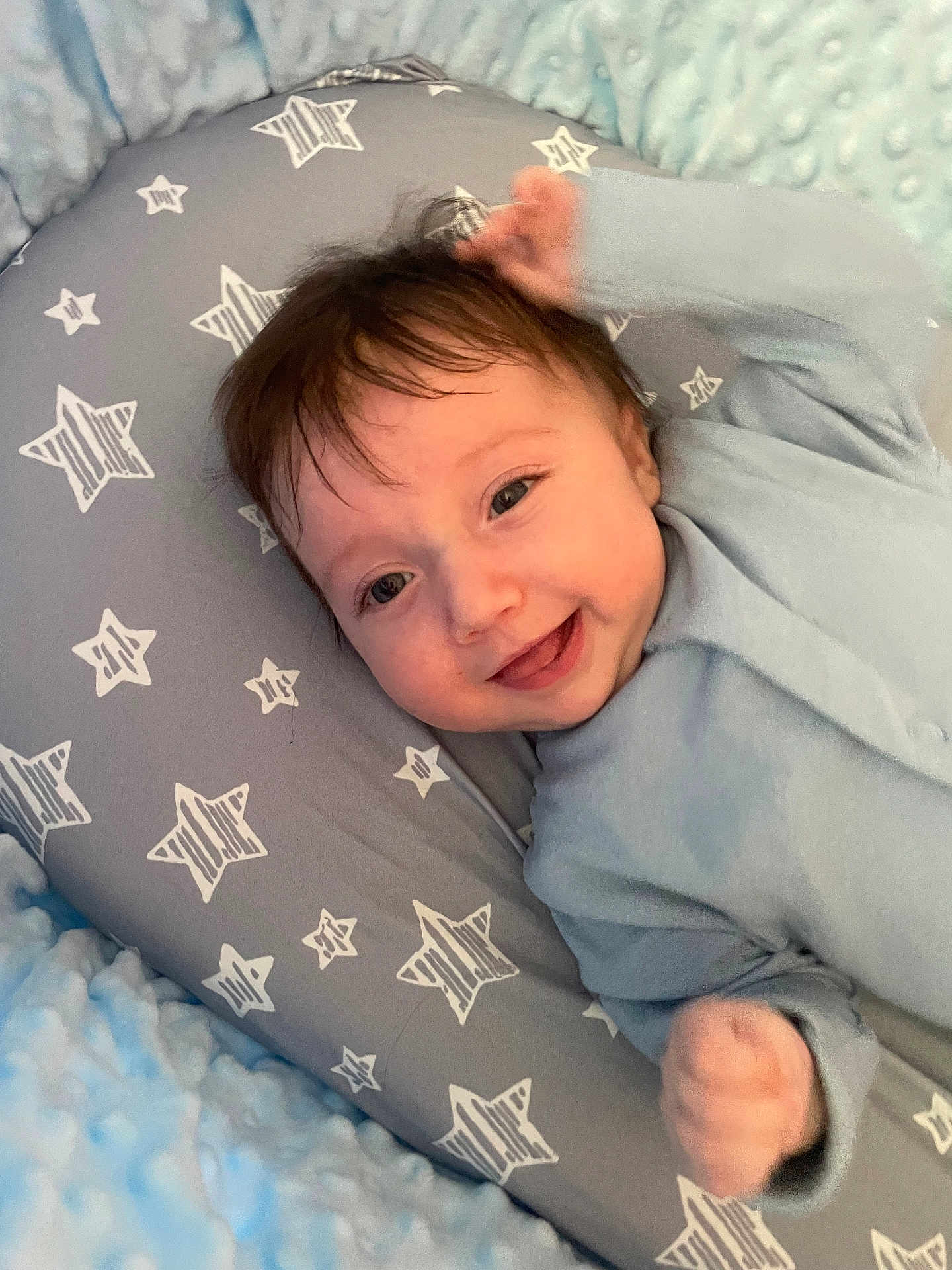Callan joined the competition — help win amazing prizes! baby, infant, smiling, blue_clothing, pillow, star_pattern, blanket, lying_down, cute, indoors, face, happy, child, soft_texture, cozy, small_hand, young, head, closeup, person