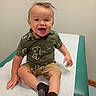 baby, child, smiling, happy, portrait, sitting, dinosaur_shirt, shorts, socks, changing_table, indoor, home, wall, chair, green, white, clothing, face, hands, photography