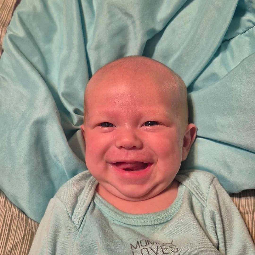 Raylin is registered to the contest to win money with this photo: baby, infant, child, smiling, happy, portrait, face, lying_down, blanket, bedding, aqua, clothing, onesie, indoor, close_up, head, eyes, mouth, cheeks, cozy