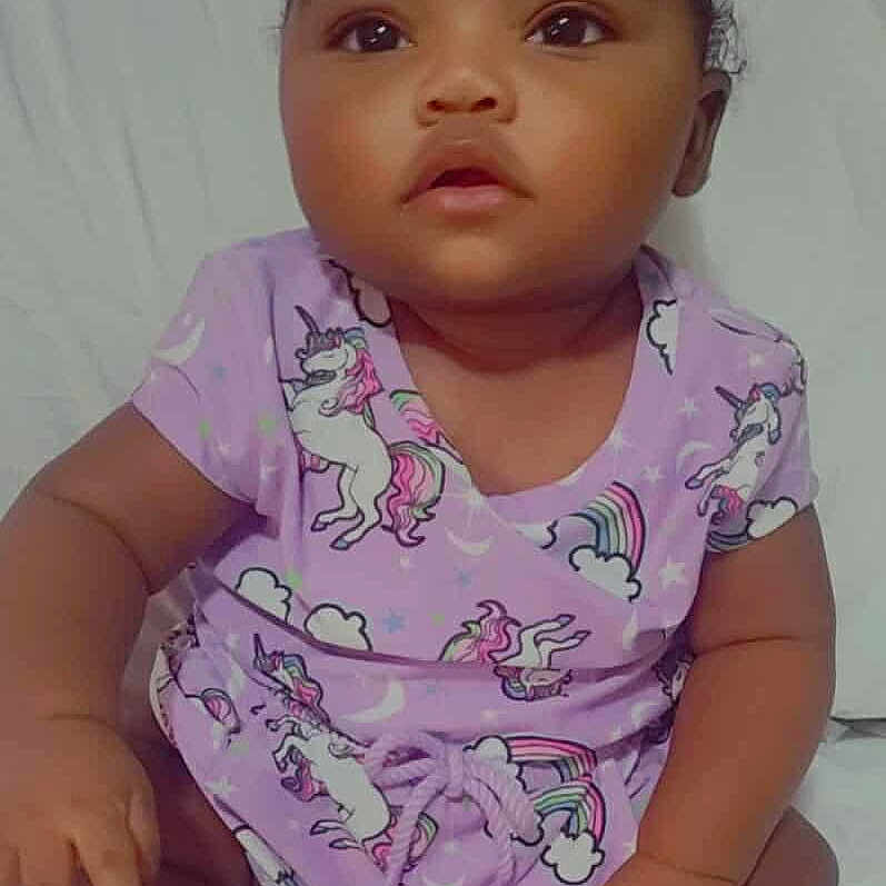 Ronoyah is registered to the contest to win money with this photo: adorable, baby, bed, bow, calm, child, clothing, curious, cute, expression, footwear, indoors, infant, person, portrait, purple_outfit, sitting, soft_lighting, unicorn, young_child