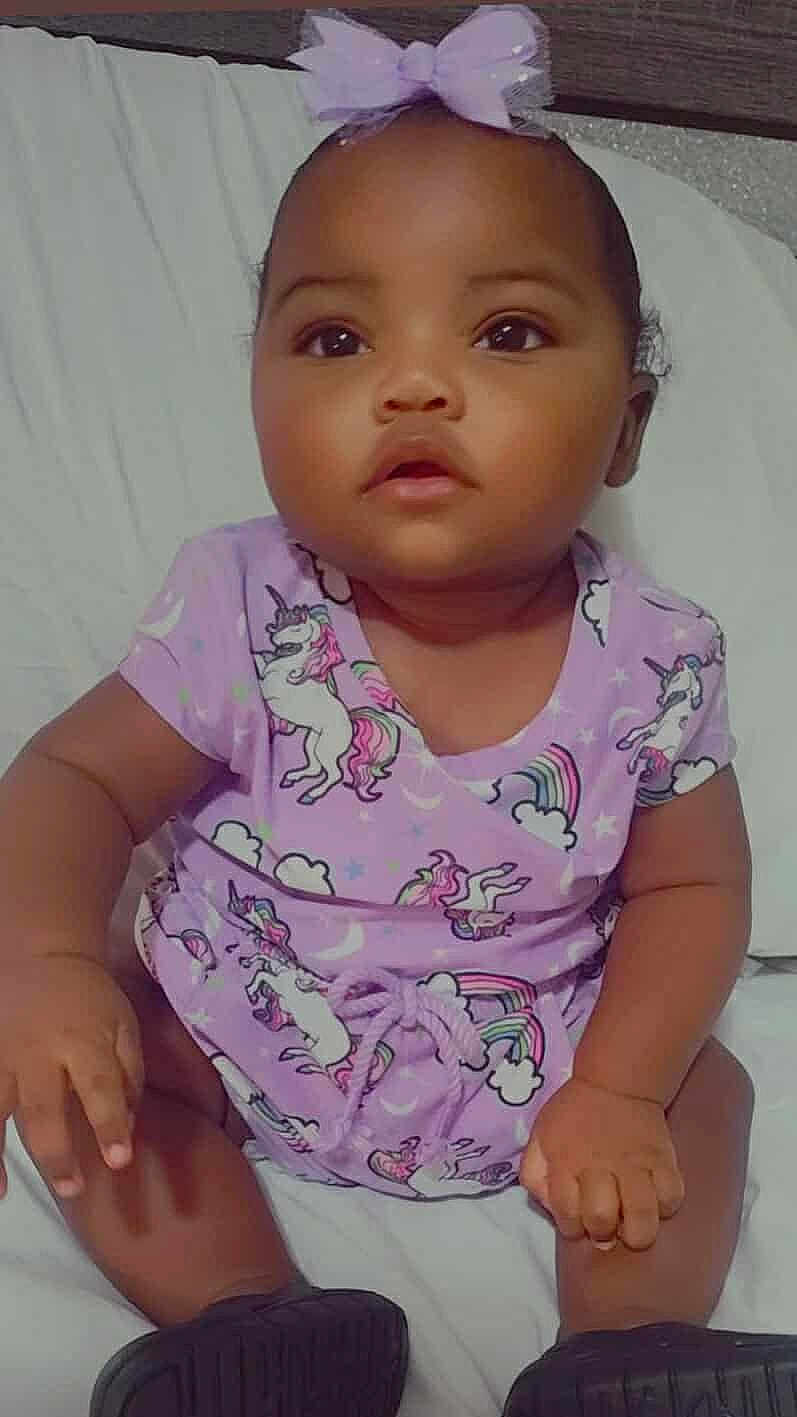 Ronoyah is registered to the contest to win money with this photo: baby, child, infant, purple_outfit, unicorn, bow, sitting, bed, cute, adorable, curious, calm, indoors, portrait, clothing, person, soft_lighting, expression, young_child, footwear