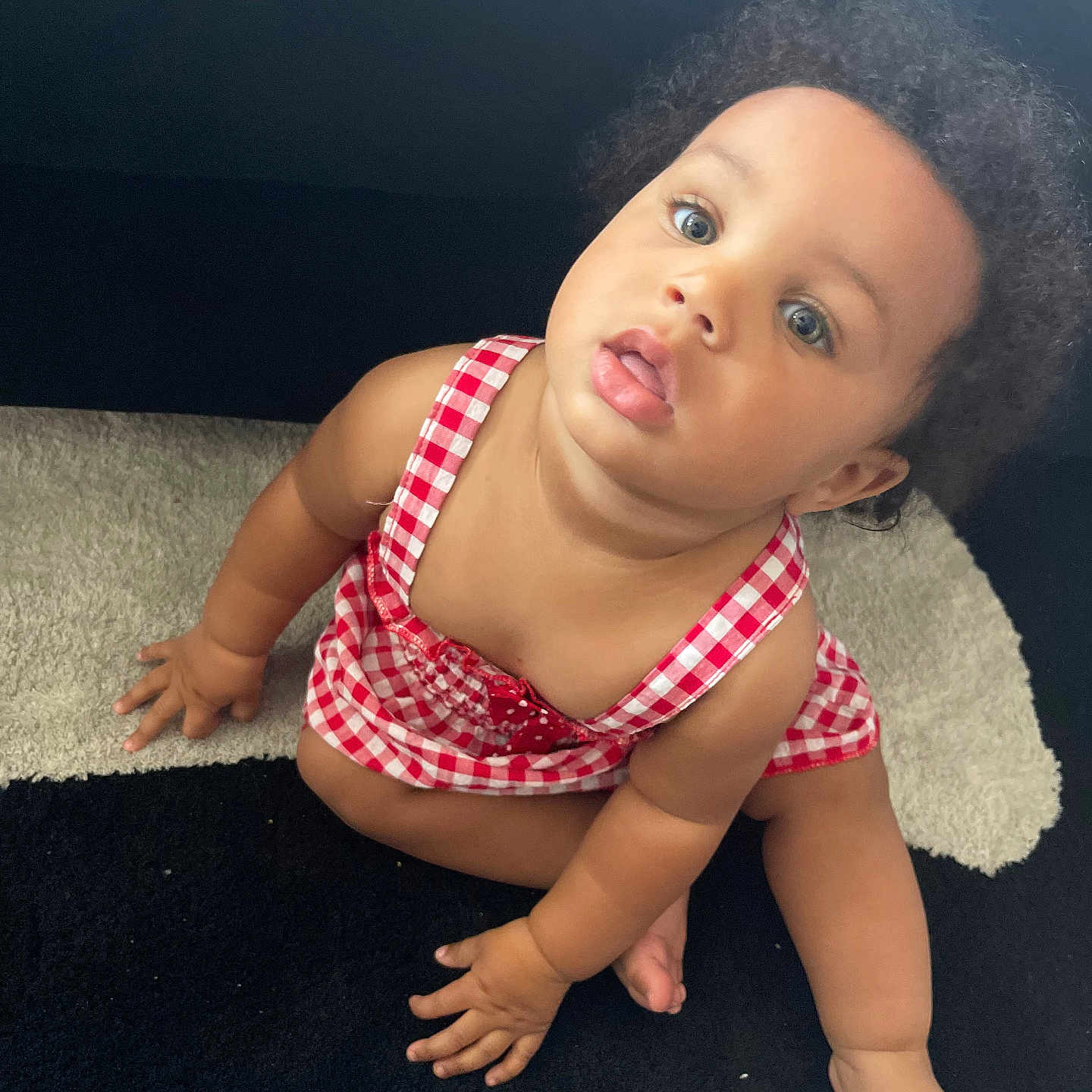Rymirrah is registered to the contest to win money with this photo: baby, barefoot, black_and_white, carpet, checkered, child, curious, curly_hair, cute, expression, foot, hand, indoor, infant, looking_up, portrait, red_dress, sitting, skin, young_child