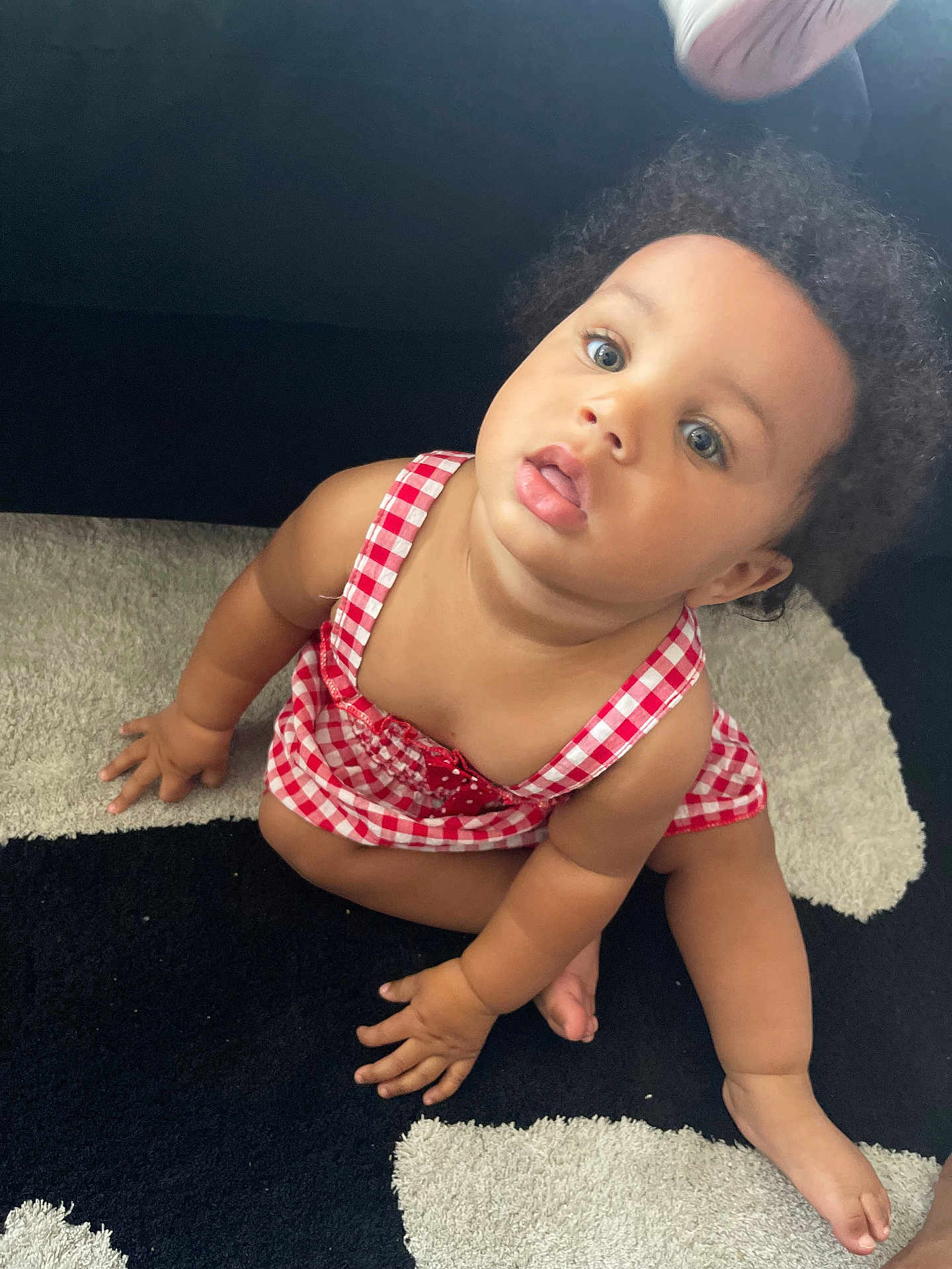 Rymirrah is registered to the contest to win money with this photo: baby, child, curly_hair, red_dress, checkered, carpet, black_and_white, sitting, looking_up, indoor, cute, infant, young_child, barefoot, skin, hand, foot, portrait, curious, expression