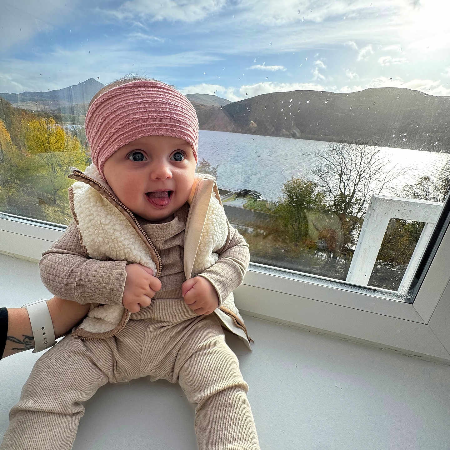 Oliwia joined the competition — help win amazing prizes! , , baby, beige_clothing, blue_eyes, child, cloudy_sky, cozy, hand, headband, lake, mountains, nature, outdoor_view, person, raindrops, sitting, smiling, tongue_out, vest, window