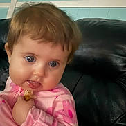 Daisy joined the competition — help win amazing prizes! baby, child, infant, portrait, sitting, couch, leather, indoor, home, pink_clothing, long_sleeves, brown_hair, blue_eyes, wide_eyed, smiling, snack, hand, face, closeup, candid