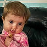 baby, child, infant, portrait, sitting, couch, leather, indoor, home, pink_clothing, long_sleeves, brown_hair, blue_eyes, wide_eyed, smiling, snack, hand, face, closeup, candid