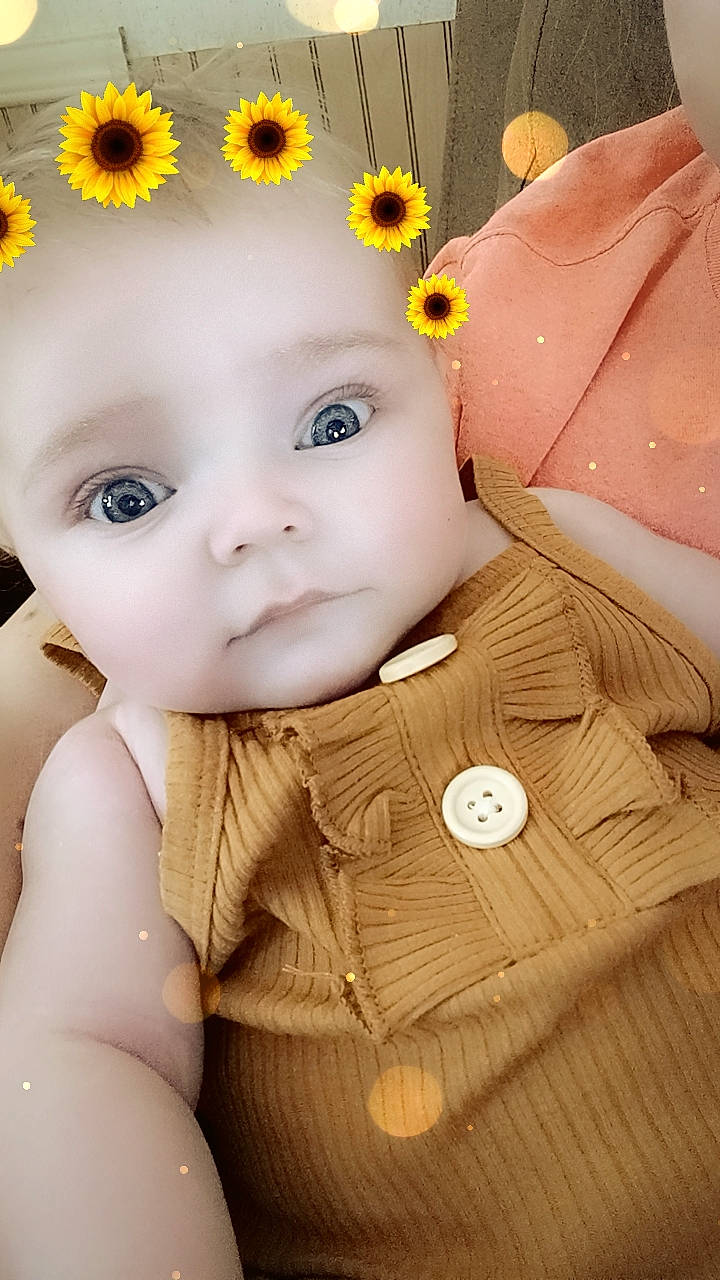 Tabby is registered to the contest to win money with this photo: baby, baby_toddler_clothing, cap, cheek, eye, face, flower, hand, happy, head, headgear, iris, person, petal, pink, plant, skin, textile, toddler, white