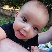 Delilah joined the competition — help win amazing prizes! baby, child, smiling, close_up, outdoor, grass, fence, trees, person, happy, cute, skin, arm, blue_eyes, black_shirt, nature, daylight, infant, portrait, expression