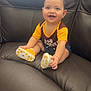 baby, smiling, child, sitting, leather_couch, yellow_shirt, polka_dot_shoes, happy, indoors, cute, short_hair, denim_shorts, small_shoes, infant, cheerful, person, portrait, seated, couch, bright