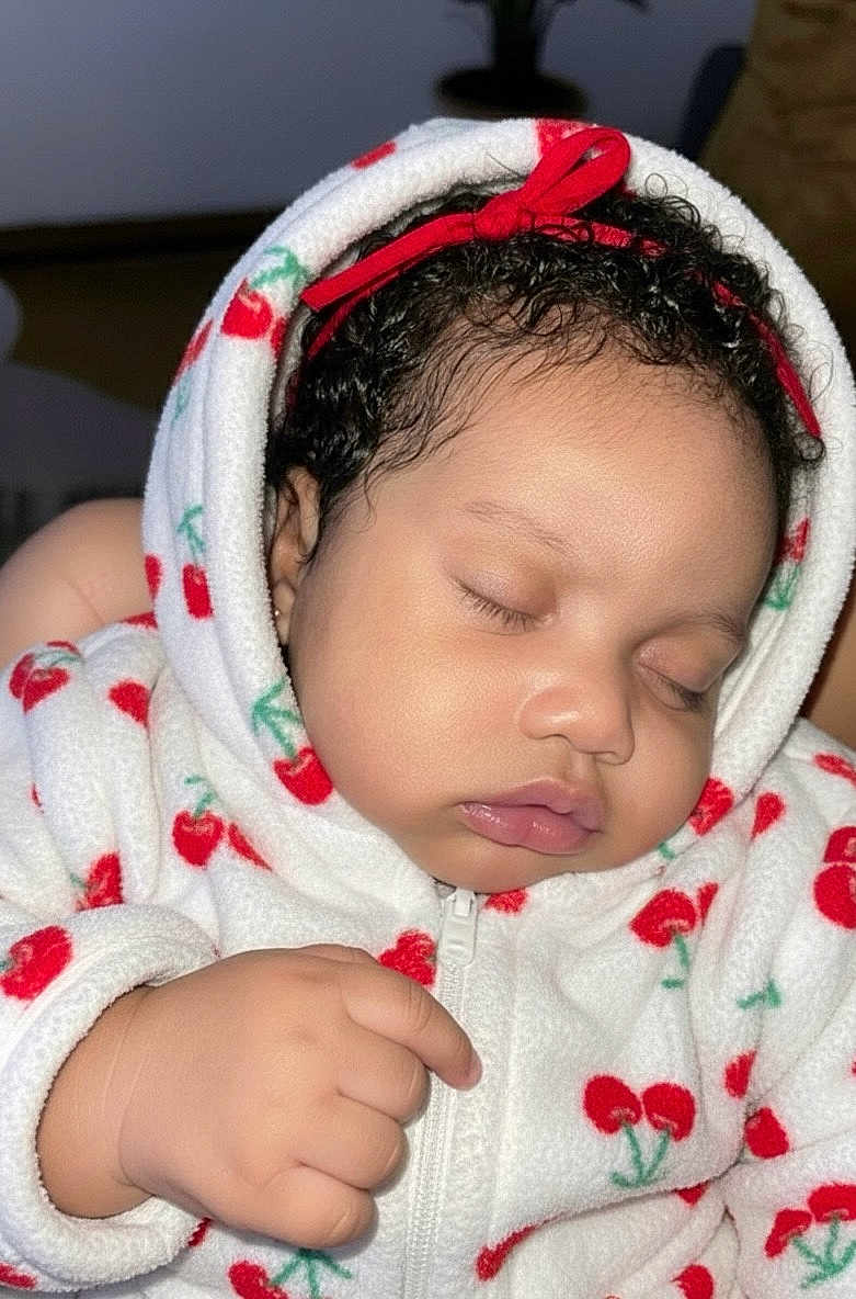 Kailly participe au concours pour gagner de l'argent avec cette photo : baby, sleeping, hoodie, cherry_pattern, red_bow, curly_hair, hand, closeup, child, infant, soft_fabric, zipper, cute, peaceful, indoor, portrait, skin, face, eyelids, cozy