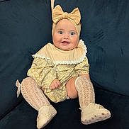Evelyn joined the competition — help win amazing prizes! baby, infant, child, smiling, headband, bow, yellow_dress, sitting, couch, blue_couch, white_shoes, knit_socks, happy, portrait, indoor, cute, fashion, person, young_child, comfortable