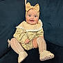 baby, infant, child, smiling, headband, bow, yellow_dress, sitting, couch, blue_couch, white_shoes, knit_socks, happy, portrait, indoor, cute, fashion, person, young_child, comfortable