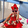toddler, child, girl, red_dress, bow, headband, sunglasses, heart_shaped, playpen, play_area, toy_mat, shoes, socks, indoor, cute, smiling, fashionable, baby, sitting, happy