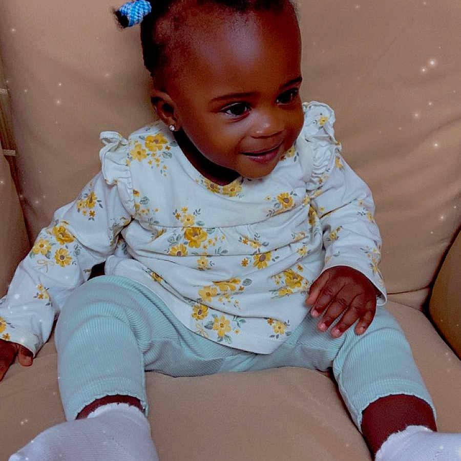Elidja participe au concours pour gagner de l'argent avec cette photo : baby, beige, child, comfortable, couch, cozy, cute, floral_clothing, hair_ties, happy, indoors, infant, long_sleeve, pants, portrait, sitting, smiling, socks, sparkle_effect, young_child