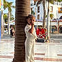 Mia participe au concours pour gagner de l'argent avec cette photo : child, pillar, white_clothing, sandals, smiling, standing, outdoor, plaza, palm_trees, bicycle, mosaic, bench, sunlight, shadows, building, windows, tiles, urban, daytime, playful