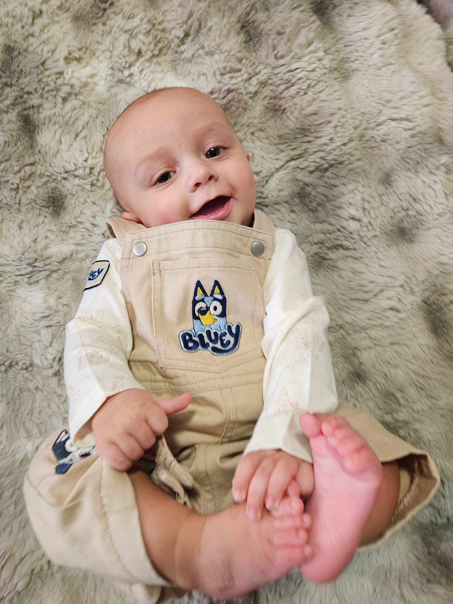 Elijah James joined the competition — help win amazing prizes! baby, infant, smile, face, head, eyes, hands, feet, barefoot, overalls, bluey_patch, beige_overalls, long_sleeve, faux_fur_blanket, texture, cozy, portrait, happy, lying_down, skin