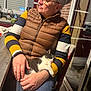 person, cat, indoor, sitting, sleeping_cat, striped_sweater, brown_vest, glasses, kitchen, chair, window, table, hand, jeans, relaxation, pet, domestic, cozy, afternoon, casual