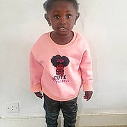 Zaynab participe au concours pour gagner de l'argent avec cette photo : child, girl, pink_sweatshirt, black_pants, black_shoes, standing, indoor, white_wall, curly_hair, high_puff, earrings, person, floor, casual_clothing, portrait, looking_at_camera, young, expression, cute, fashion