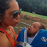 Nayeli is registered to the contest to win money with this photo: woman, baby, life_jacket, sunglasses, river, water, outdoor, nature, trees, grass, park, child, person, summer, daylight, portrait, closeup, expression, bonding, family