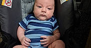 Brendan joined the competition — help win amazing prizes! baby, blue_striped_onesie, car_seat, child, clothing, cute, dim_lighting, face, footwear, hands, indoors, infant, legs, person, portrait, relaxed, sitting, warning_label, wooden_background, young