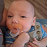 Brendan is registered to the contest to win money with this photo: baby, button, child, closeup, clothing, cute, eyes, face, floor, hand, indoor, infant, overalls, pacifier, person, portrait, skin, sleepy, striped_shirt, wood