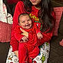 baby, celebration, christmas_theme, couch, cozy, family, festive, happy, holding, holiday_pajamas, home, indoor, infant, long_hair, person, pillow, plaid_shoes, red_clothing, smile, woman