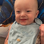 Roman joined the competition — help win amazing prizes! baby, smile, bib, pillow, hand, tattoo, infant, face, clothing, pattern, blue, gold, couch, happy, skin, eyes, mouth, person, indoor, cute