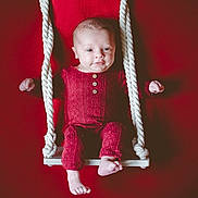 Lou participe au concours pour gagner de l'argent avec cette photo : baby, infant, swing, red_background, red_clothing, knitwear, ropes, feet, hands, face, portrait, indoor, cute, child, smile, seated, white_swing, expression, young, cozy