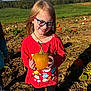 child, girl, pumpkin, glasses, red_shirt, outdoor, pumpkin_patch, smiling, fall, nature, field, greenery, sunlight, happy, person, long_hair, casual_clothing, daytime, grass, vegetable