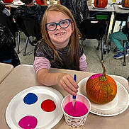 Sarah is registered to the contest to win money with this photo: child, glasses, painting, pumpkin, classroom, paintbrush, paint, cup, plate, table, smile, apron, art, kids, school, desk, plastic_apron, orange_pumpkin, creative_activity, happy