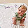 baby, child, infant, portrait, sitting, smiling, curious, red_hair, bow, green_outfit, romper, blanket, personalized_blanket, fish_pattern, indoor, carpet, home, cute, barefoot, photography