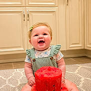 Izabella is registered to the contest to win money with this photo: baby, child, infant, smiling, happy, portrait, watermelon, fruit_cake, birthday, cake, sitting, indoor, kitchen, cabinets, rug, green_overalls, floral_shirt, hair_bow, bare_feet, celebration