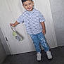 child, boy, smile, striped_shirt, blue_jeans, sneakers, indoor, door, floor_tiles, holding_object, casual_clothing, happy, portrait, standing, short_hair, young, person, clothing, footwear, light_background