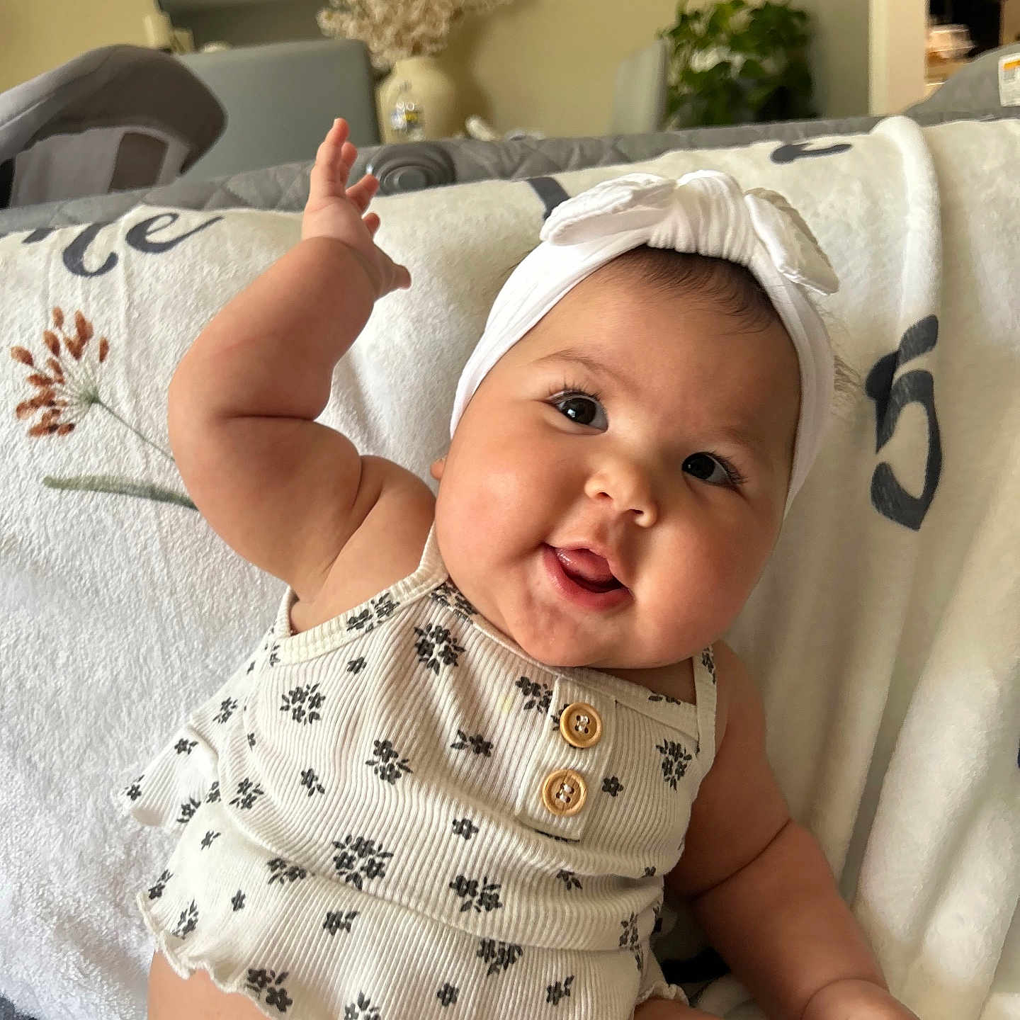 Sage is registered to the contest to win money with this photo: baby, infant, headband, smile, arm, cheeks, clothing, blanket, indoor, furniture, couch, plant, mirror, vase, happy, cute, portrait, child, person, home
