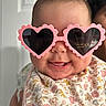 Sage is registered to the contest to win money with this photo: baby, sunglasses, heart_shaped, pink, drool, smiling, bib, floral_pattern, indoor, face, head, person, close_up, cute, child, fashion_accessory, happy, portrait, infant, clothing