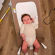 Bryan is registered to the contest to win money with this photo: baby, infant, baby_seat, wooden_floor, white_onesie, socks, face, hair, floor, furniture, household_item, mop, cable, relaxing, indoor, person, child, smiling, cute, small
