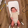 baby, infant, baby_seat, wooden_floor, white_onesie, socks, face, hair, floor, furniture, household_item, mop, cable, relaxing, indoor, person, child, smiling, cute, small