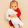 baby, infant, red_clothing, stuffed_animal, white_bunny, plush_toy, cute, portrait, child, soft_texture, barefoot, innocence, looking_at_camera, indoor, neutral_background, small_hands, young_child, cozy, adorable, toddler