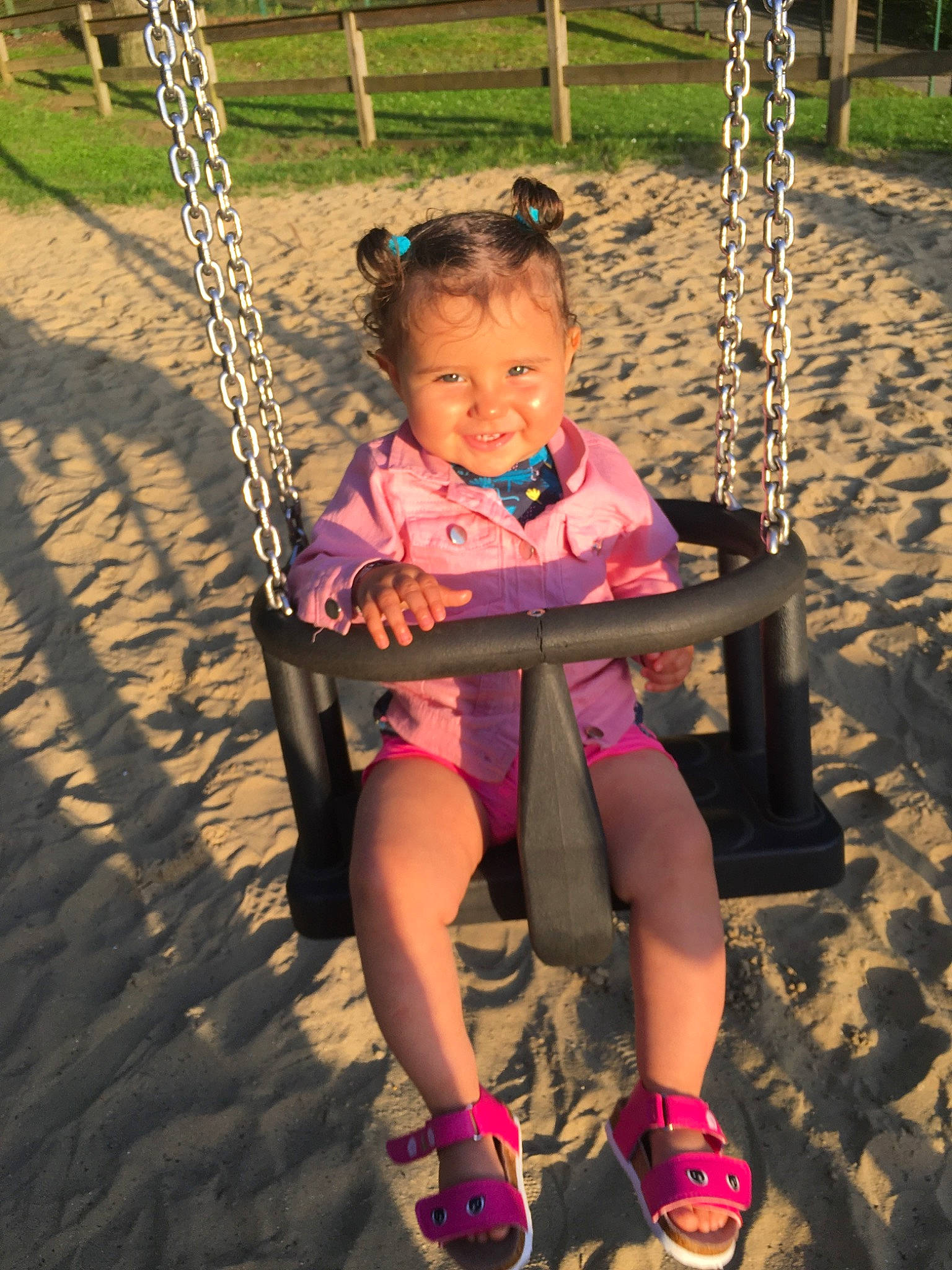 Lyzie participe au concours pour gagner de l'argent avec cette photo : child, city, fun, grass, happy, joy, leisure, outdoor_play_equipment, people_in_nature, person, pink, play, playground, public_space, recreation, sandal, sitting, smile, swing, toddler