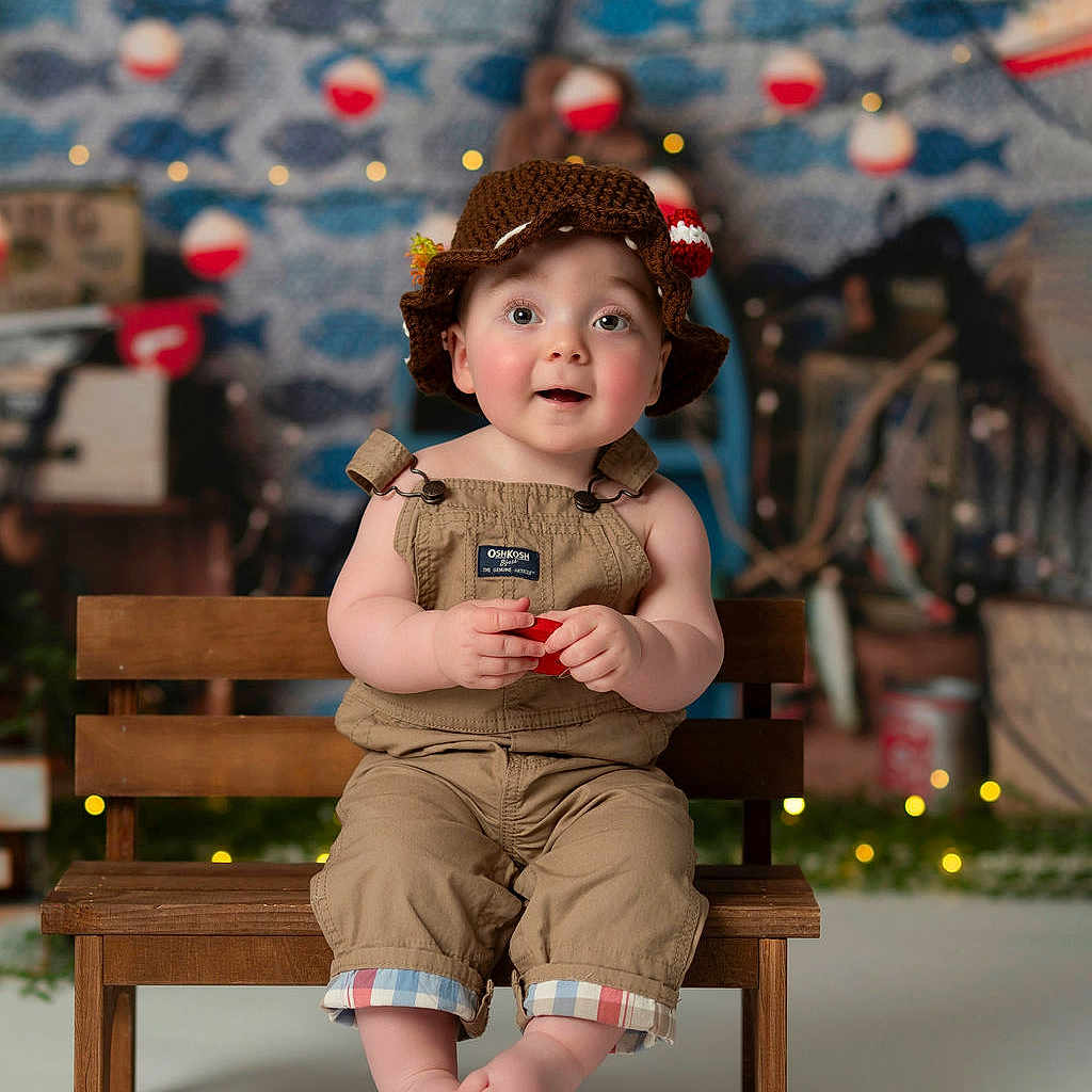 Arlo is registered to the contest to win money with this photo: baby, background, bench, child, clothing, crocheted_hat, cute, decorations, eyes, face, feet, hat, indoor, lights, overalls, photo_studio, portrait, smiling, toy, wooden_bench