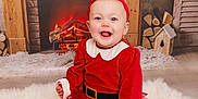 Brooklyn joined the competition — help win amazing prizes! baby, child, red_clothing, headband, smile, happy, indoor, fireplace, holiday, festive, rug, fur_rug, decor, wood, log, toy_house, floor, toddler, portrait, cute