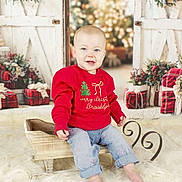 Brooklyn is registered to the contest to win money with this photo: baby, barefoot, child, christmas, cozy, decorations, festive, fur_rug, happy, holiday, indoor, jeans, portrait, presents, red_sweater, sitting, sled, smiling, wooden, wreath