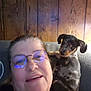 Buster joined the competition — help win amazing prizes! woman, glasses, dog, puppy, dachshund, pet, shoulder, smile, indoor, wooden_wall, couch, casual, person, face, portrait, companion, cozy, home, relaxation, friendly