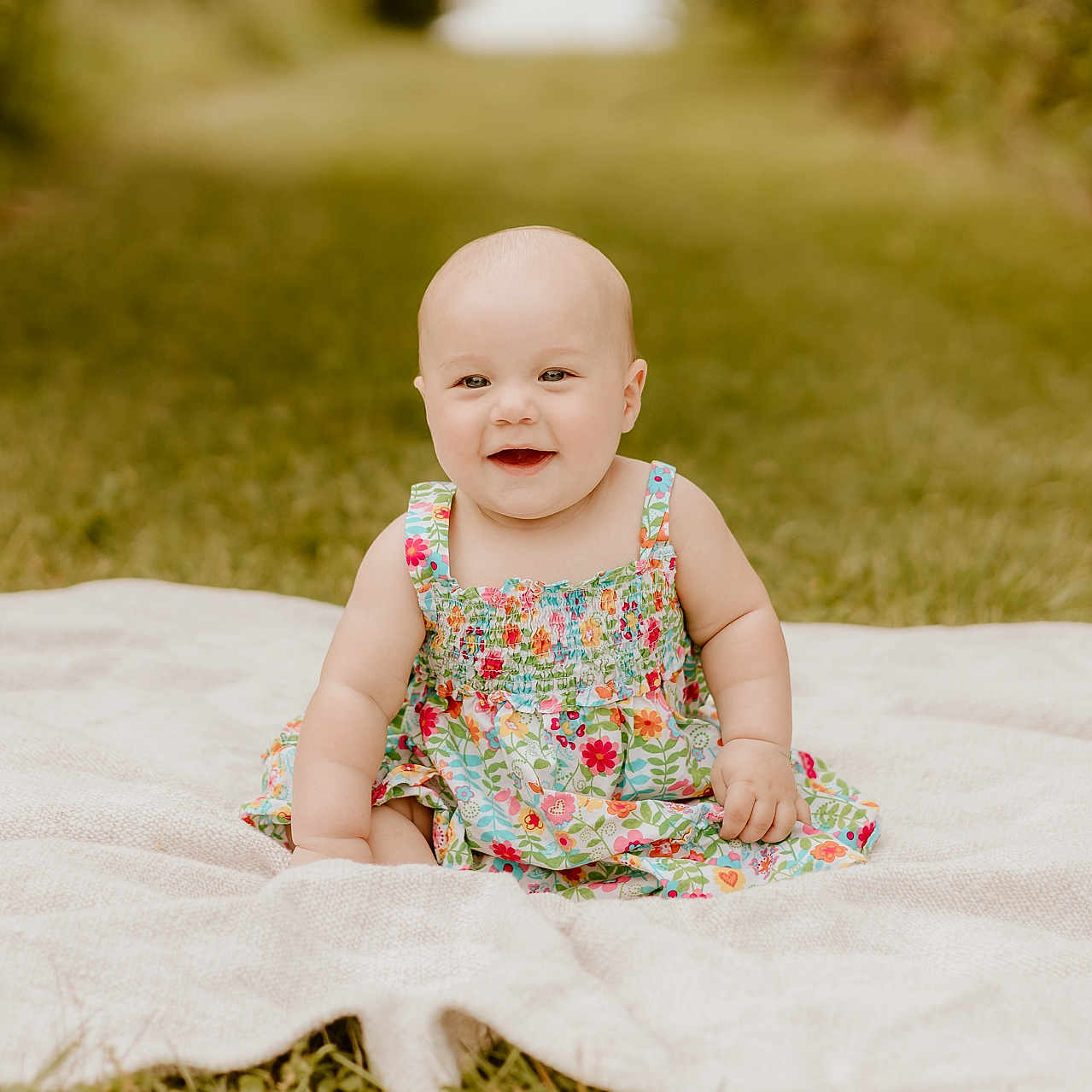 Oaklie is registered to the contest to win money with this photo: baby, blanket, child, cute, daylight, dress, floral_pattern, grass, greenery, happy, head, infant, nature, outdoor, portrait, sitting, skin, smiling, summer, young_child