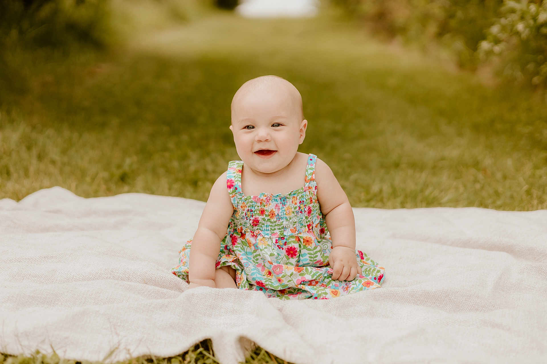 Oaklie is registered to the contest to win money with this photo: baby, child, smiling, sitting, blanket, outdoor, grass, dress, floral_pattern, happy, cute, portrait, infant, nature, greenery, summer, daylight, young_child, skin, head
