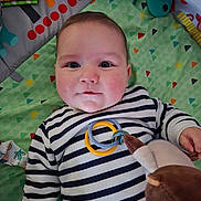 Elliott a rejoint le concours — aidez-le/la à gagner de superbes lots ! baby, infant, play_mat, striped_clothing, plush_toy, toy, child, smiling, face, hand, colorful, patterned, indoors, cute, young, lying_down, soft_toys, cheeks, casual, bright