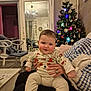 Elliott participe au concours pour gagner de l'argent avec cette photo : baby, child, infant, pajamas, hands, christmas_tree, decorations, mirror, chandelier, living_room, furniture, blanket, cozy, smile, person, indoor, holiday, festive, warm, cute