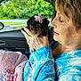 affection, blanket, blue_shirt, car_interior, close_up, cozy, cute, dog, flower_accessory, greenery, hand, holding, love, nature, pet, pink_blanket, portrait, puppy, window, woman