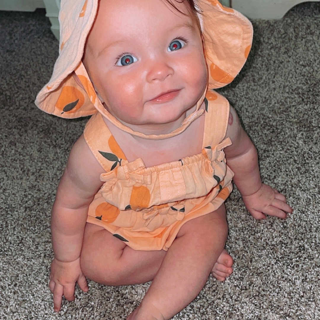 Graylynn is registered to the contest to win money with this photo: baby, bonnet, cap, clothing, costume, crawling, door, dress, face, hardwood, hat, head, hood, pants, person, photography, portrait, sitting, sunhat, wood