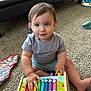 toddler, child, toy, xylophone, colorful, carpet, indoor, smiling, sitting, gray_shirt, blue_shorts, playtime, furniture, couch, floor, person, cute, hands, happy, young